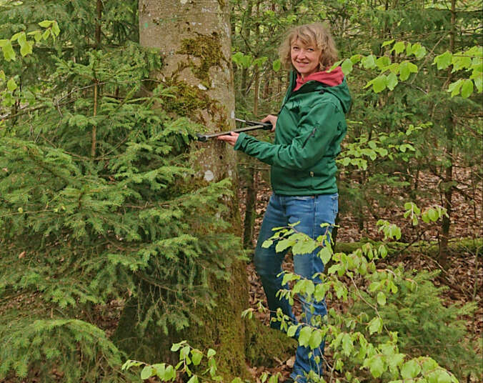 Frau mit grüner Jacke steht vor einem Baum.